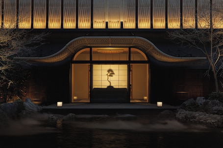 A traditional building with a curved roof, a water feature in front, and a view of the interior through a large window.