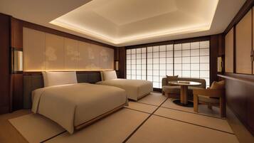 A hotel room with two beds, a sitting area with a table and chairs, a large window with a view, and a ceiling with recessed lighting.