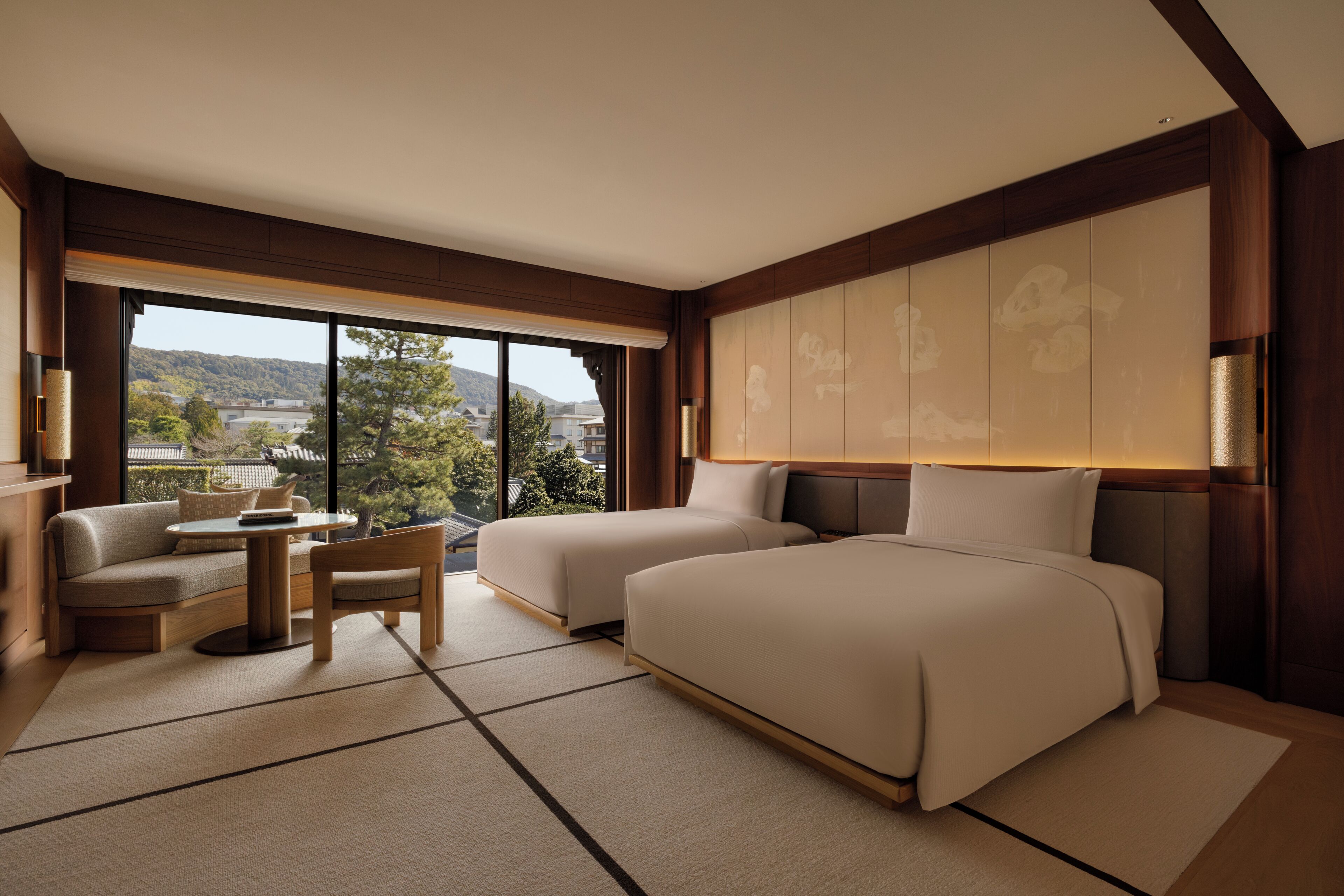 A hotel room with a sofa, two beds, a small table, and a view of the outdoors.