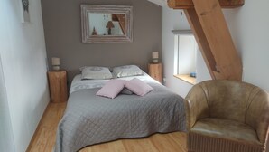 Ein Schlafzimmer mit einem Bett, zwei Nachttischen, einem Sessel, einem Fenster und einem Spiegel an der Wand.