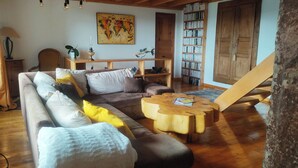 Ein gemütliches Wohnzimmer mit einem Ecksofa, einem Holztisch und einem Bücherregal voller Bücher.
