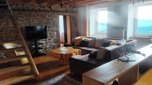 Ein gemütliches Wohnzimmer mit Steinwand, einer Holztreppe, einem Flachbildfernseher, einer Couch mit Kissen und einem Holztisch.