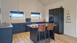 Una cucina moderna con isola centrale, due lampade a sospensione, forno incassato e mobili scuri.