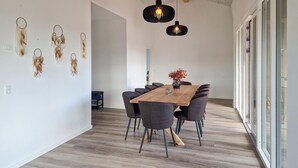 Zona pranzo moderna con tavolo in legno e sedie scure, un vaso con fiori e dreamcatcher appesi al muro.