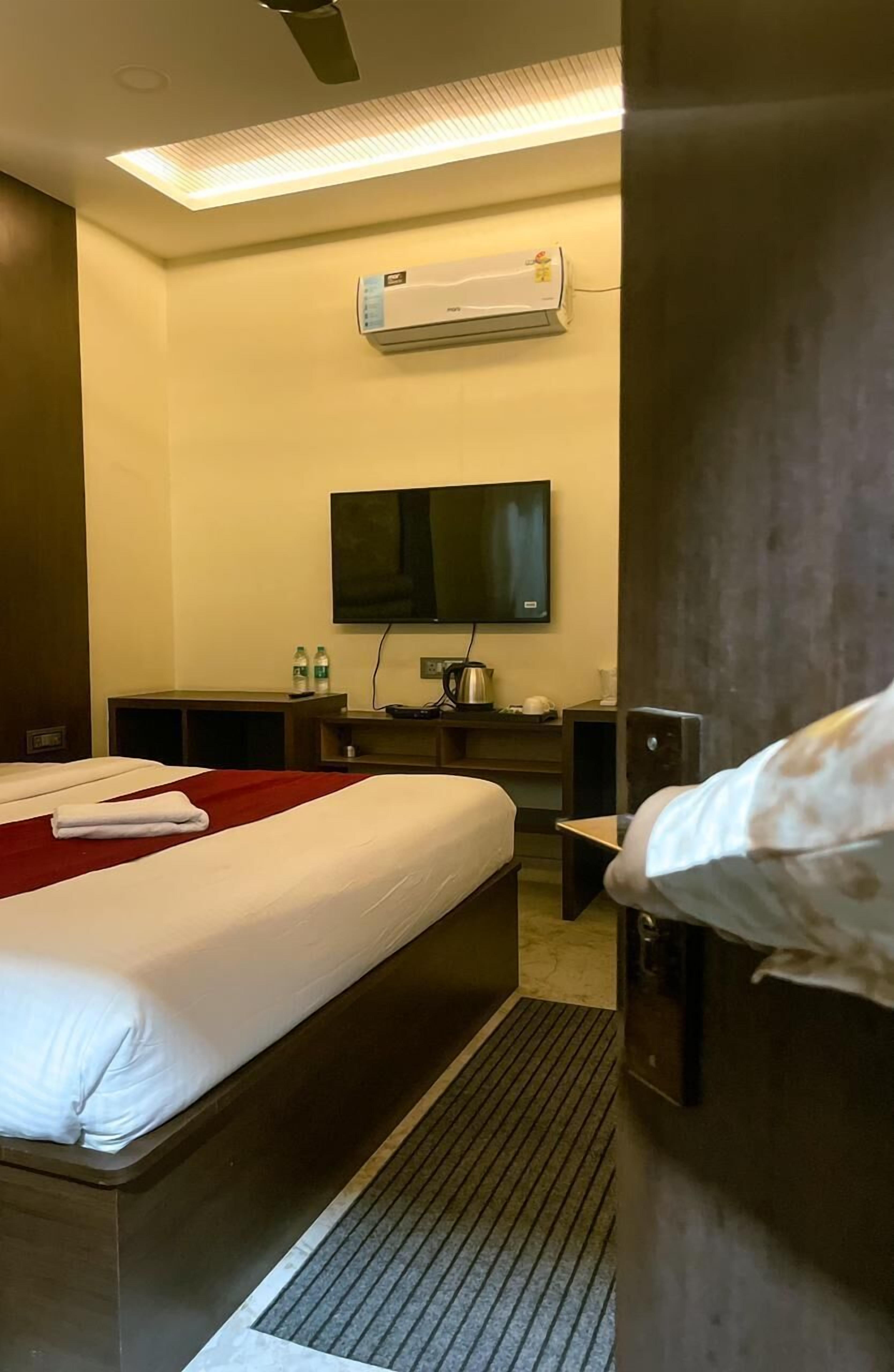 Habitación de hotel con dos camas, un televisor de pantalla plana, equipo de aire acondicionado, un escritorio con silla y una mesita con tetera y tazas.