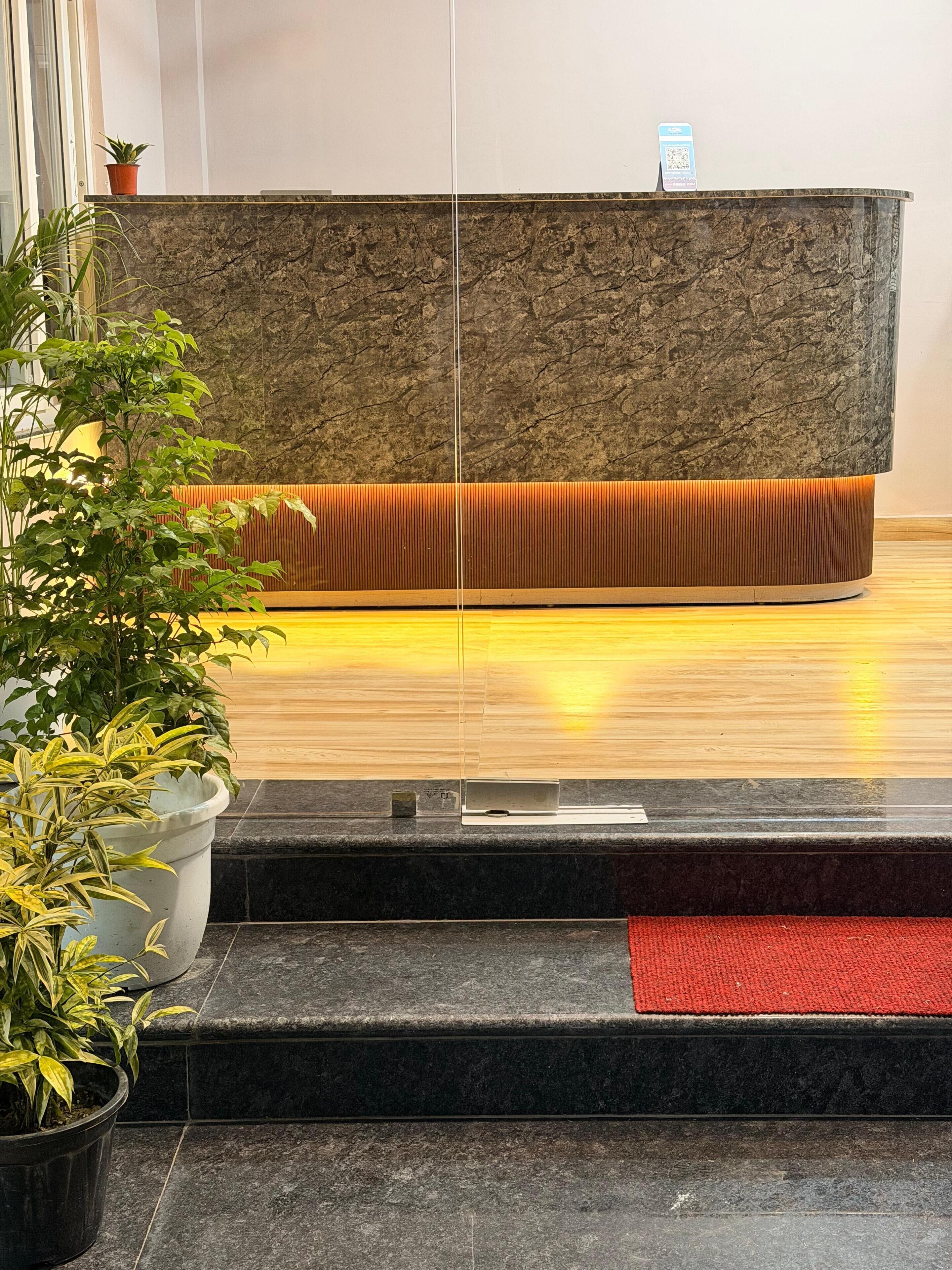 Un espace d’accueil avec un comptoir de réception en marbre, une moquette rouge et des plantes en pot.