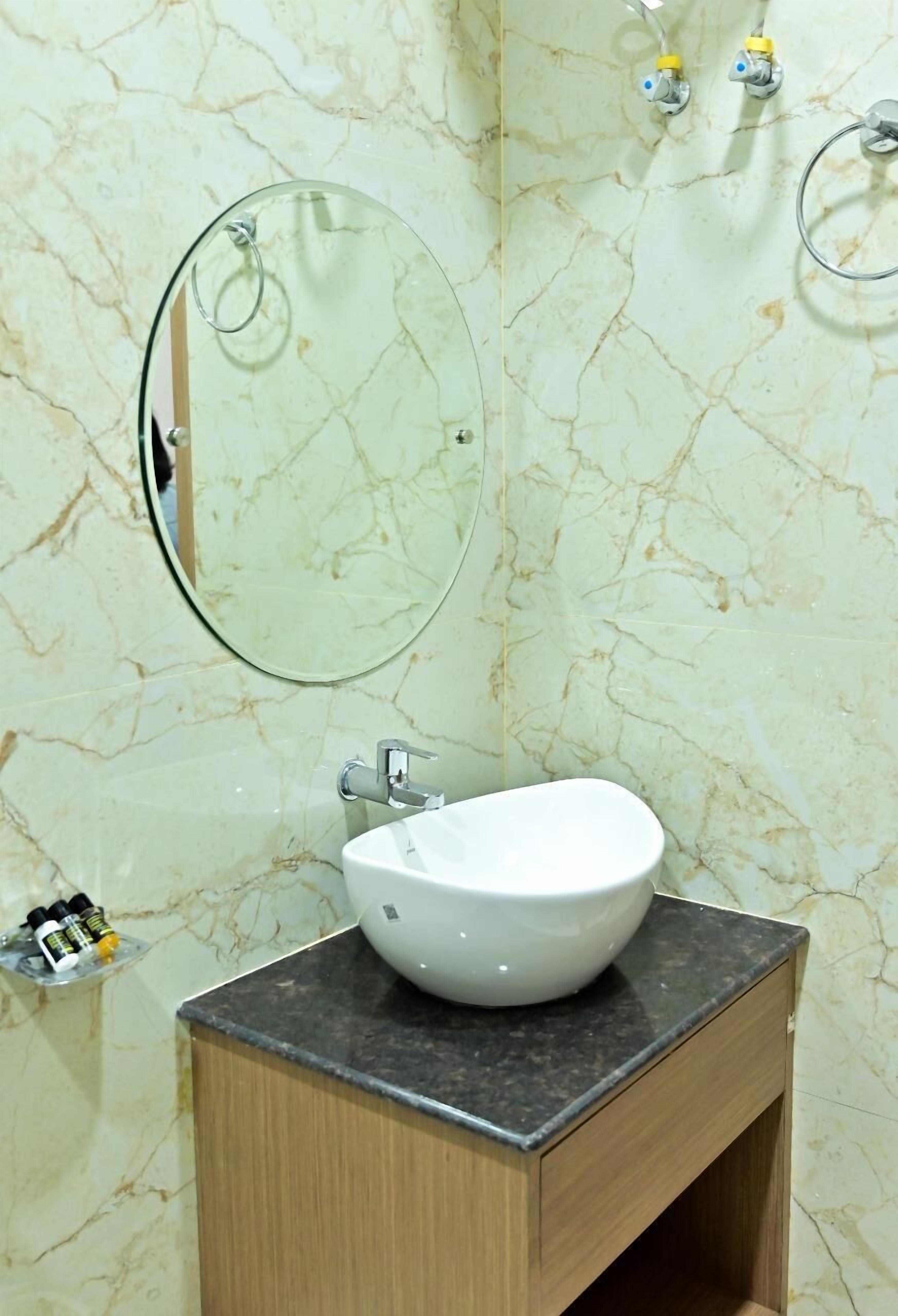 Un baño con pared de mármol, un espejo redondo, un lavabo blanco y un armario de madera.