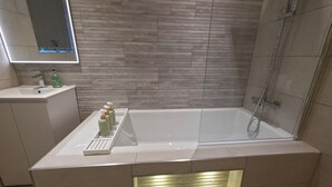 Ein modernes Badezimmer mit einer weißen Badewanne, einer Duschkabine und einem Waschtisch mit Spiegel.
