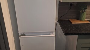 Ein weißer Kühlschrank in einer Küche mit schwarzer Arbeitsplatte und grünen Schränken.
