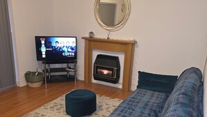 Ein Wohnzimmer mit einer Couch, einem Fernseher, einem Kamin und einem Spiegel an der Wand.