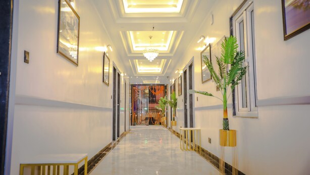A hotel corridor with a marble floor, framed artwork, and potted plants. - Hotel Shri Ram Ratan Inn (Ayodhya)