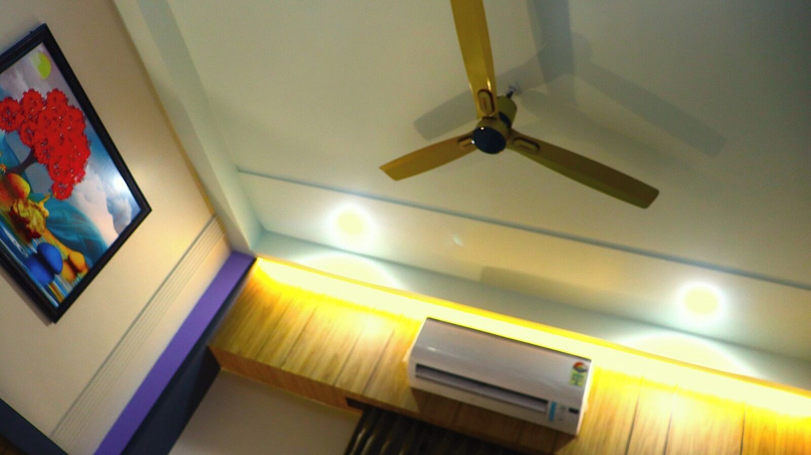 Dans la pièce, on trouve un ventilateur de plafond, des spots encastrés et un climatiseur fixé au mur.
