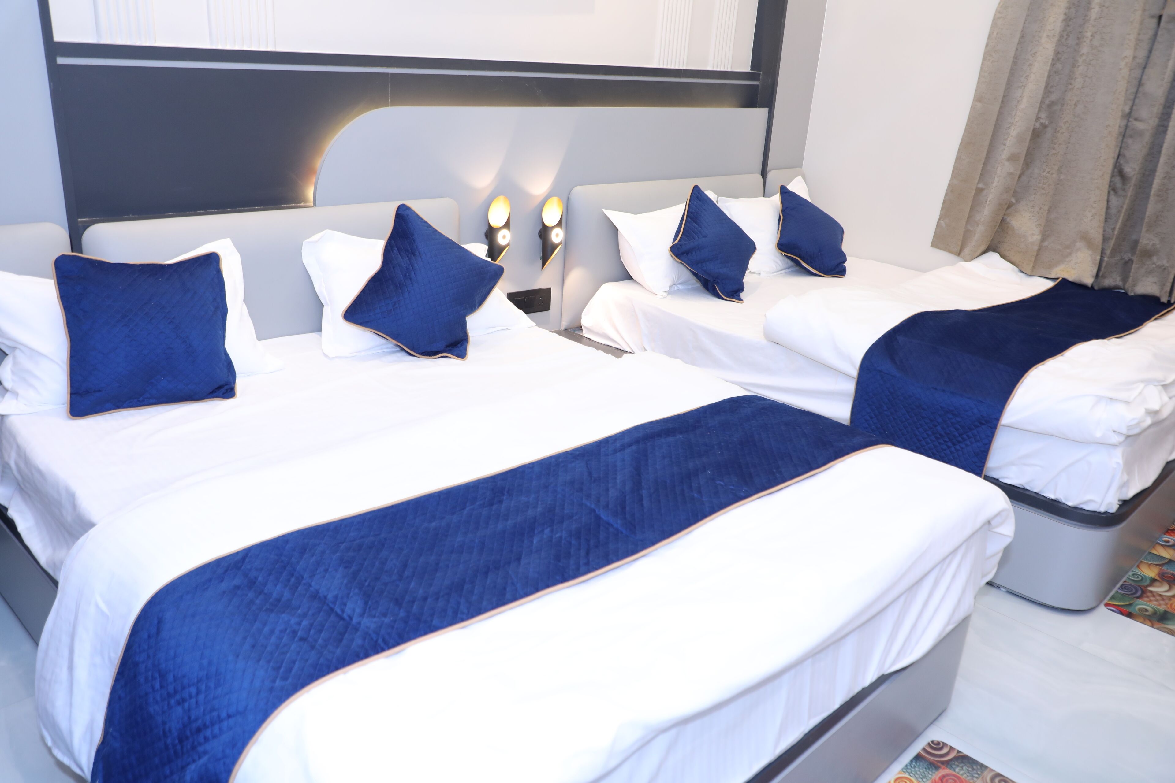 A hotel room with two beds, each with white bedding and blue accents, and a headboard with built-in lighting.