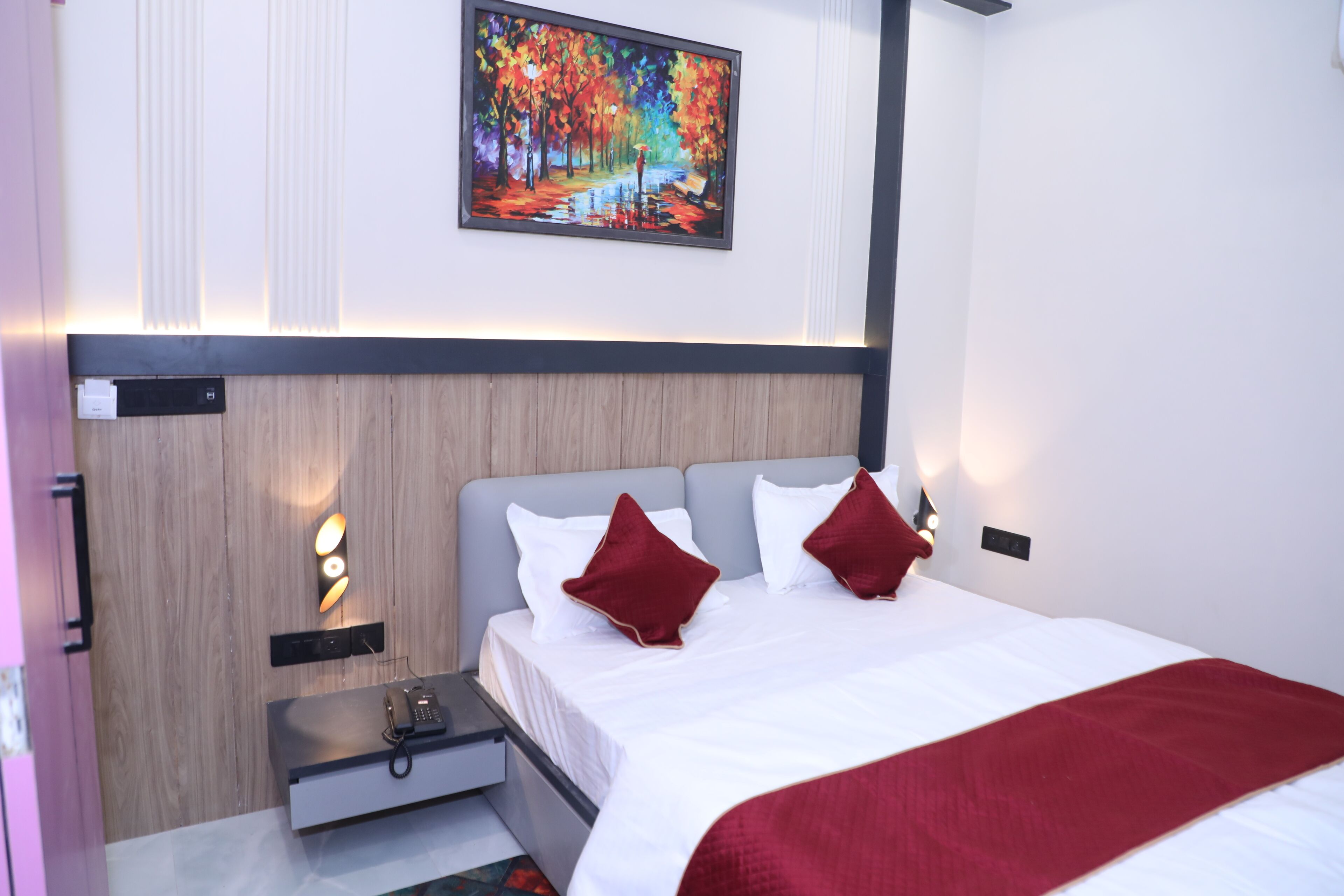 A modern hotel room with a neatly made bed, a bedside table with a phone, and a painting on the wall.