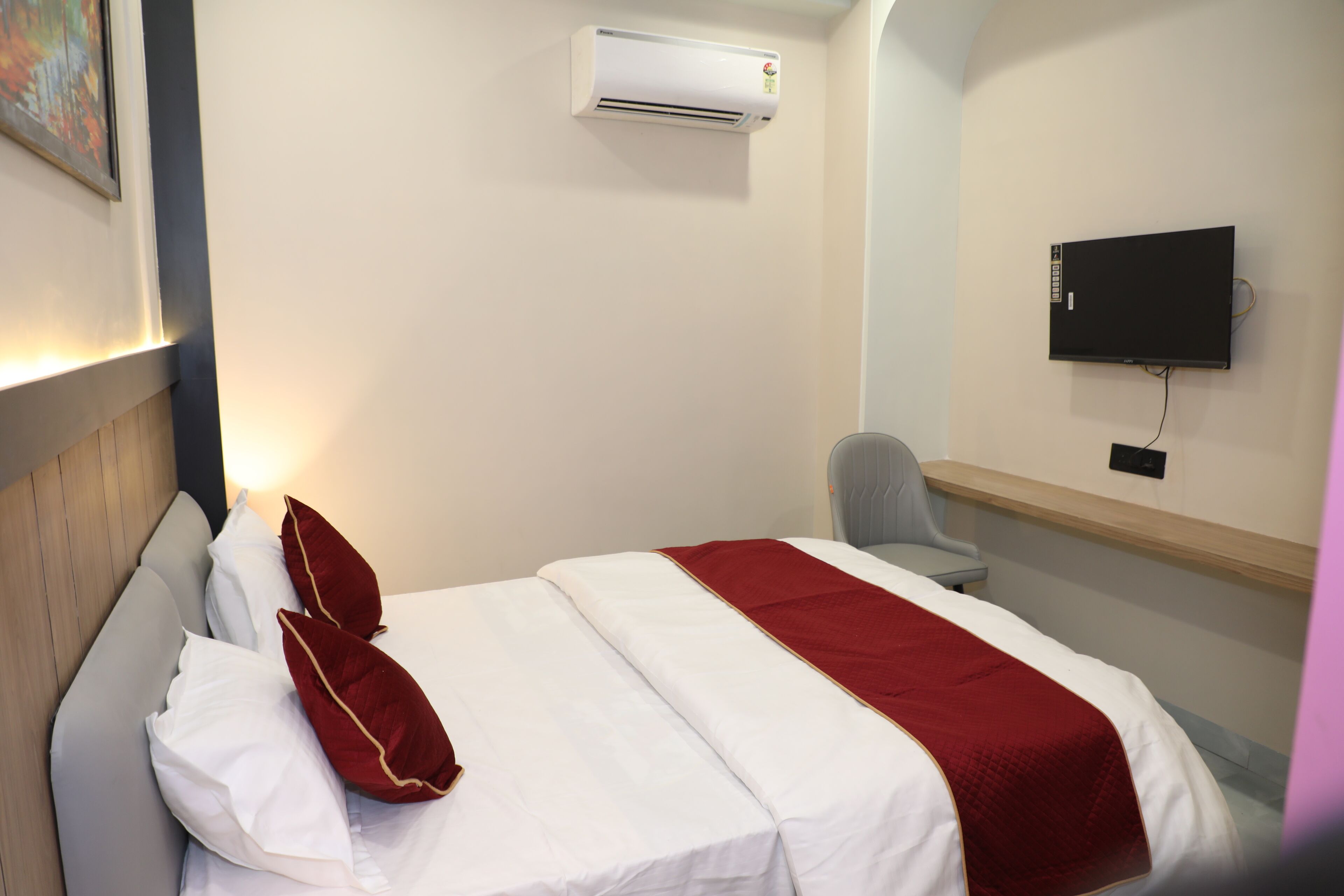 A hotel room with a bed, a chair, a TV, and an air conditioning unit.