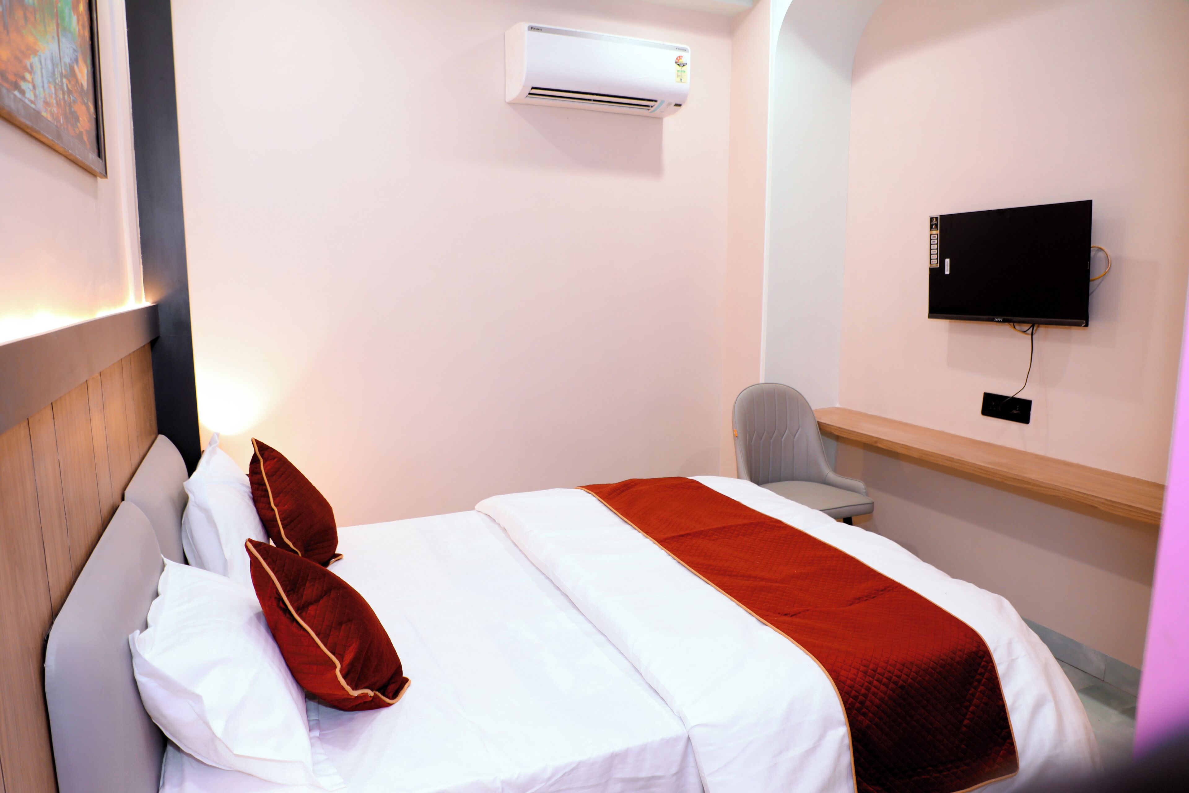 A hotel room with a bed, an air conditioning unit, a television, and a chair.