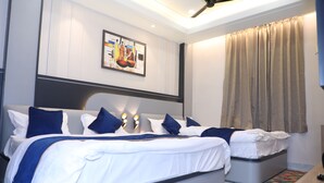 A modern hotel room with two beds, a ceiling fan, a painting on the wall, and a large window with curtains. - Hotel Shri Ram Ratan Inn (Ayodhya)