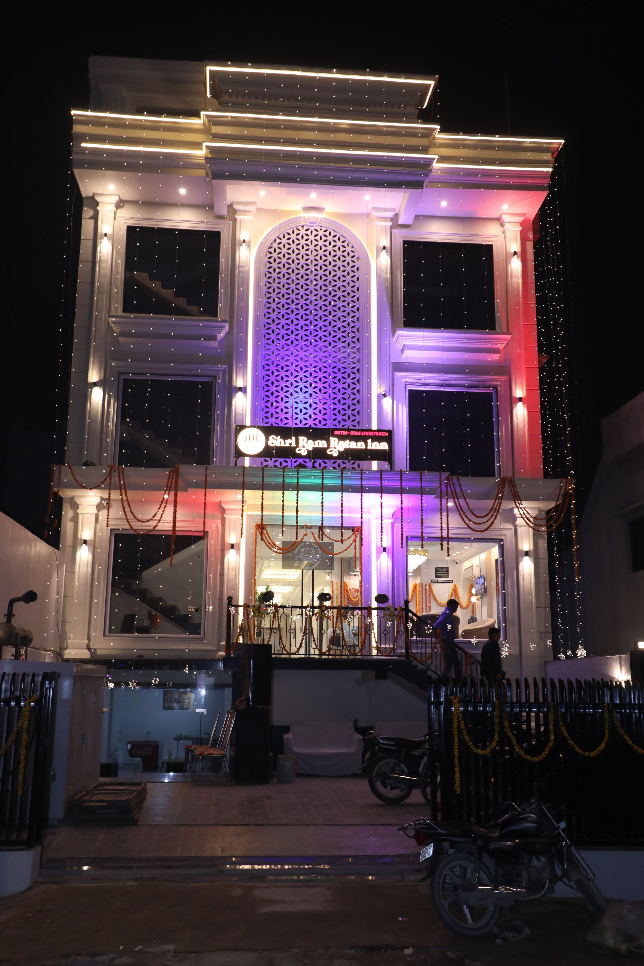 A hotel with a sign reading "Shri Rama Rajan Hotel." It features a large entrance with a staircase, a decorative arch, and a well-lit facade.
