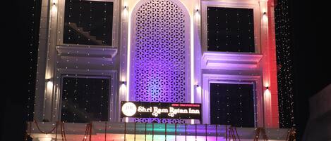 A hotel with a sign reading "Shri Rama Rajan Hotel." It features a large entrance with a staircase, a decorative arch, and a well-lit facade.