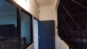 Un couloir étroit avec une porte bleue fermée, un mur de verre d’un côté et une rambarde métallique de l’autre.