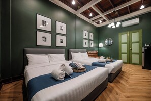 Habitación de hotel con dos camas, suelo de madera, paredes verdes y cuadros en la pared.