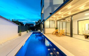 A modern outdoor pool area with a clear blue pool, adjacent lounge chairs, and a glass-enclosed patio. - Nice apartment in Zadar with heated swimming pool (Zadar)