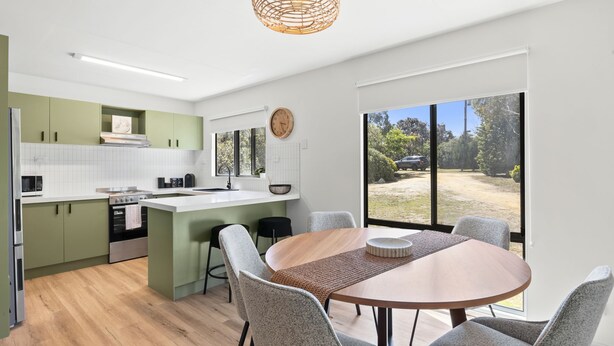 A modern kitchen with a central island, dining area with chairs, and a large window offering a view of the outdoors.