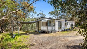 A mobile home with a porch, surrounded by trees and a gravel path.