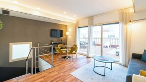 A modern hotel room with a wooden floor, a balcony with outdoor furniture, a TV, and a dining area with yellow chairs. - Placa Catalunya gran duplex (Barcelona)