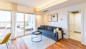 A modern living room with a grey sofa, a round coffee table, and a large sliding glass door leading to an outdoor seating area. - Placa Catalunya gran duplex (Barcelona)
