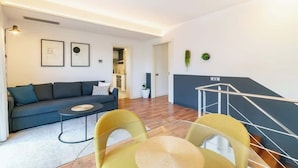 A modern living room with a sofa, coffee table, and chairs, a staircase, and framed artwork on the wall. - Placa Catalunya gran duplex (Barcelona)