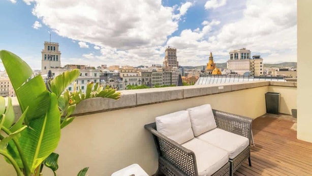 A balcony with wicker furniture, a view of city buildings, and a clear sky. - Placa Catalunya gran duplex (Barcelona)