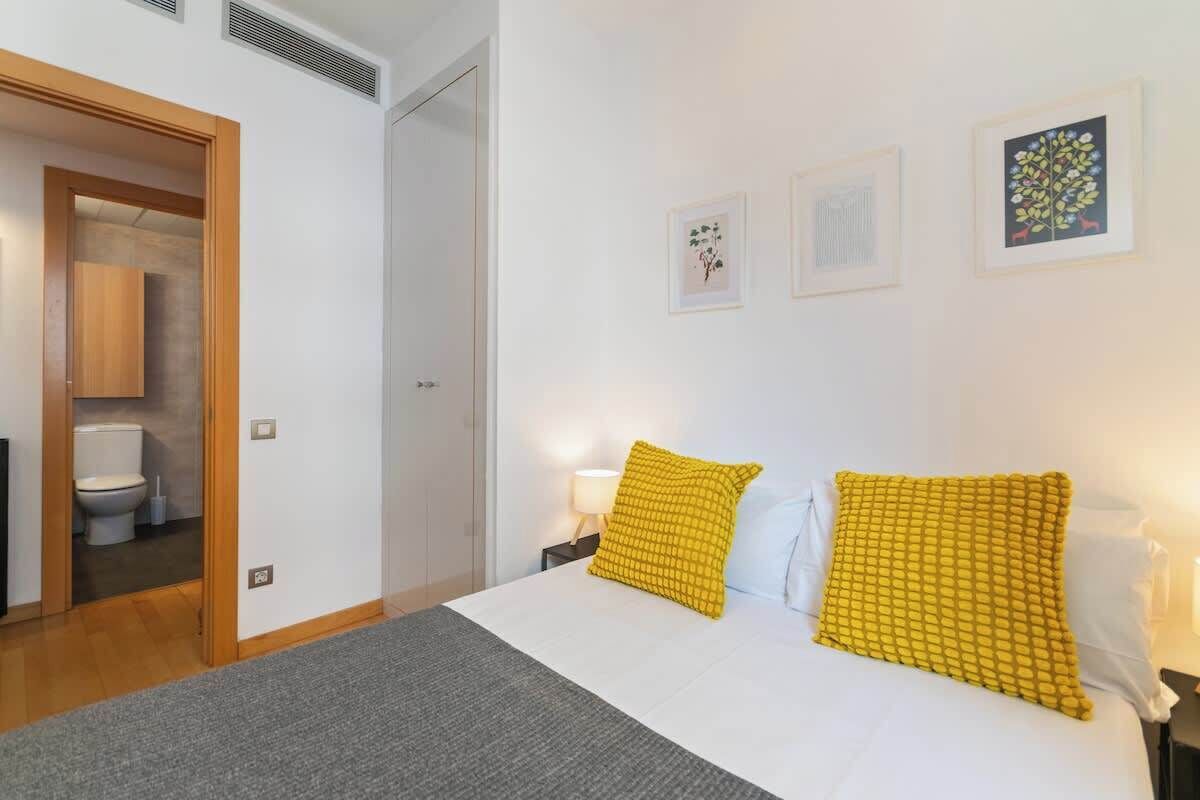 A hotel room with a bed, a bedside table with a lamp, and a door leading to a bathroom.
