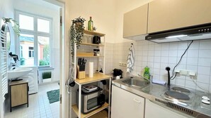 Une cuisine moderne avec des armoires blanches, un plan de travail en acier inoxydable et un four encastré. Une fenêtre offre une vue sur l’extérieur, et une plante est posée sur le plan de travail.
