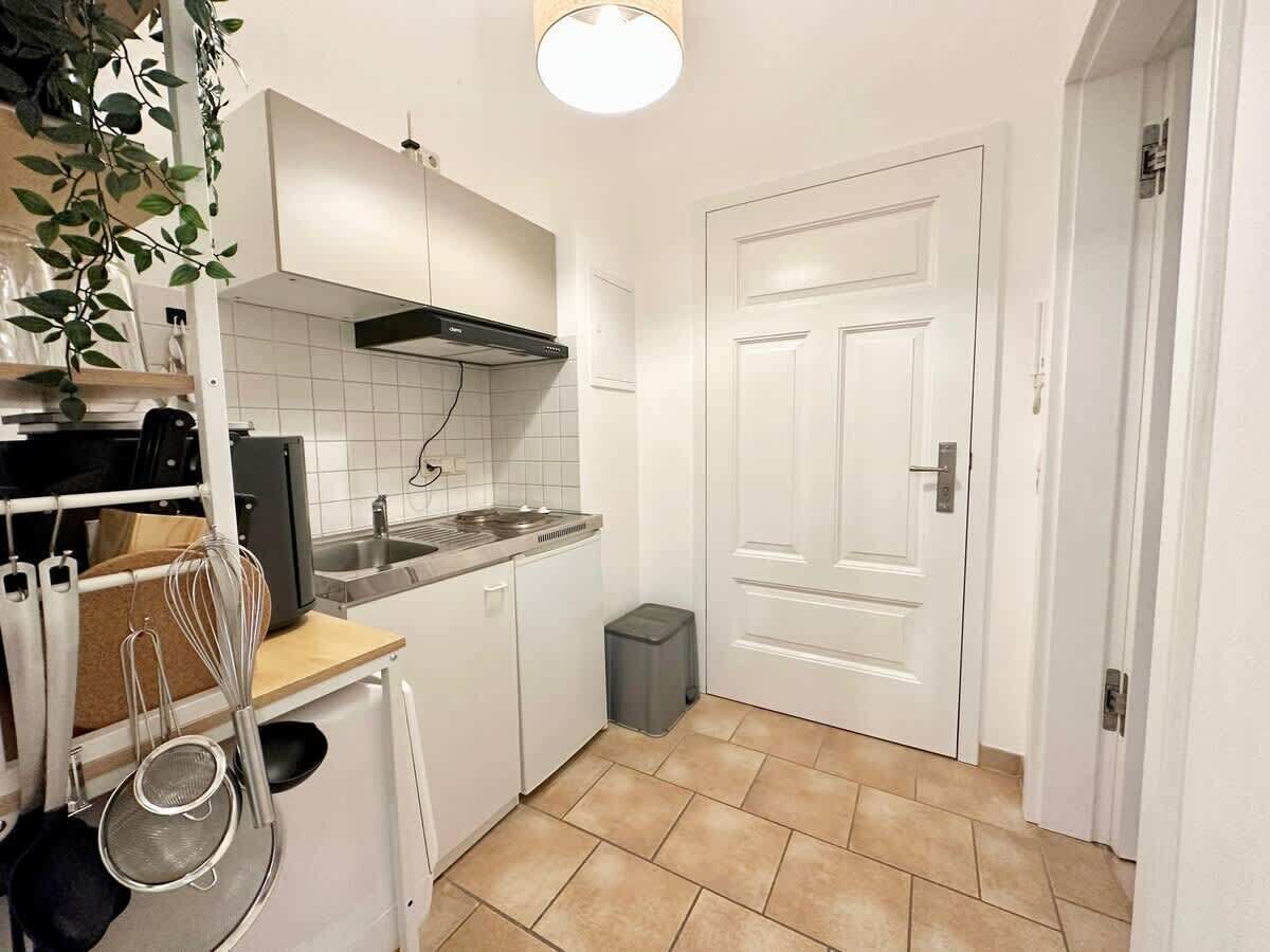 A compact kitchen with white cabinets, a stainless steel sink, and a small trash bin.