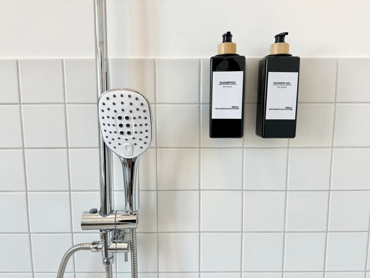A shower with a handheld showerhead and two bottles of shower gel on a tiled wall.