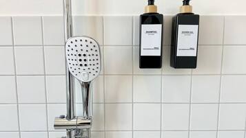 A shower with a handheld showerhead and two bottles of shower gel on a tiled wall.