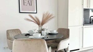A modern dining area with a round table, two chairs, and a decorative wall piece.