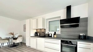 A modern kitchen with white cabinetry, a built-in oven, and a window with blinds.