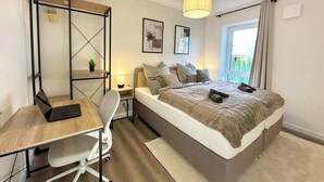 Ein Schlafzimmer mit Bett, Schreibtisch, Stuhl, Lampe und Fenster.