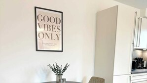 Ein Essbereich mit einem runden Tisch, vier Stühlen, einem gerahmten Zitat an der Wand und einer Küche im Hintergrund.