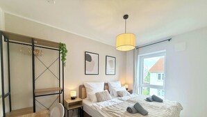 Ein modernes Schlafzimmer mit Bett, Nachttischen, einem Schreibtisch und einem Fenster mit Blick auf Gebäude.