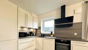 Eine moderne Küche mit weißen Schränken, einem Einbauofen und einem Fenster, das für natürliches Licht sorgt.