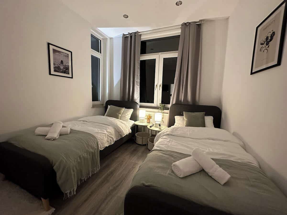 Ein Hotelzimmer mit zwei Einzelbetten, einem kleinen runden Tisch und einem Fenster mit Vorhängen.