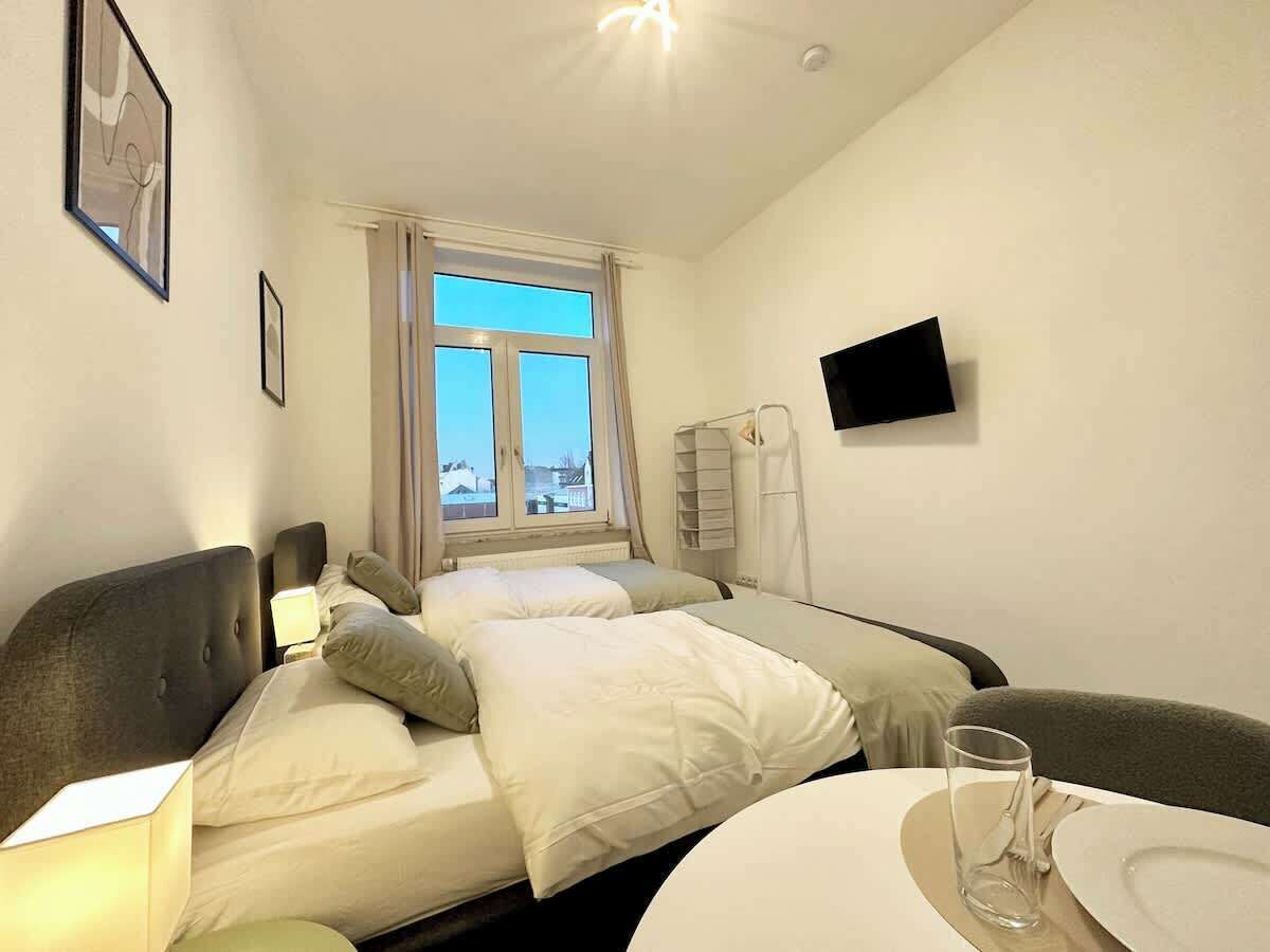 Habitación de hotel con dos camas, televisión, ventana con vistas y zona de comedor con mesa y sillas.