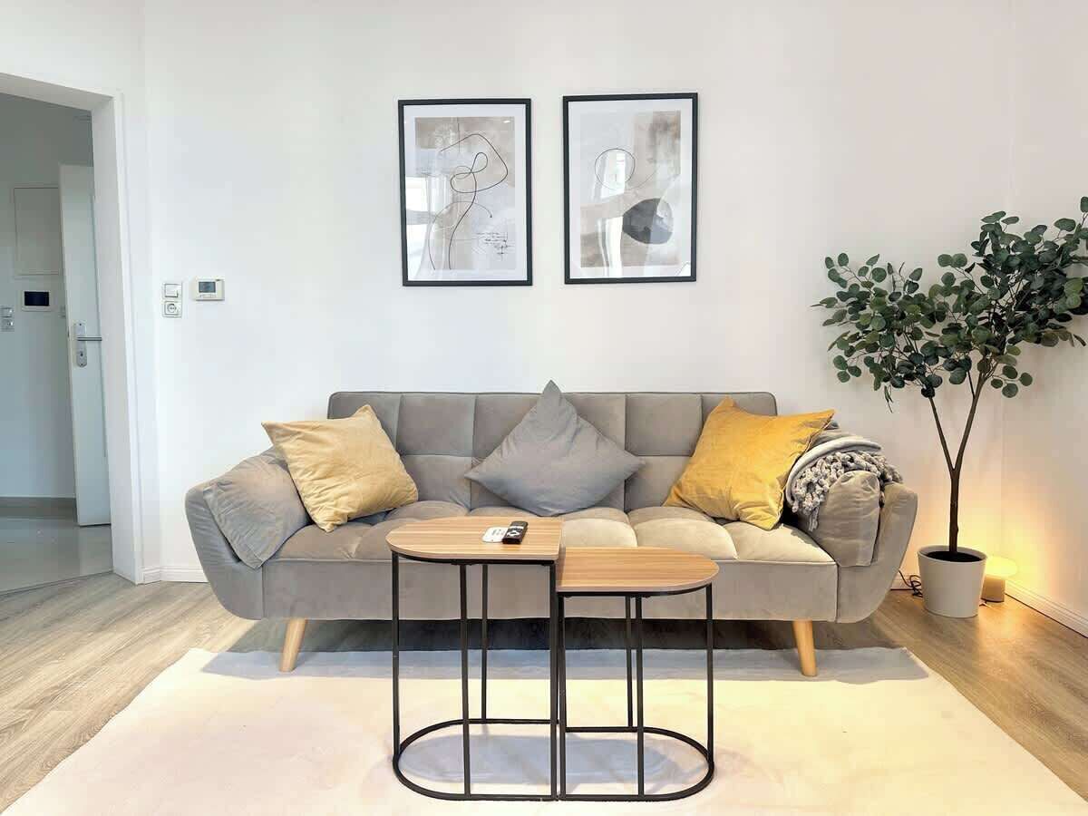 Ein modernes Wohnzimmer mit grauem Sofa, zwei Beistelltischen und einer Zimmerpflanze.