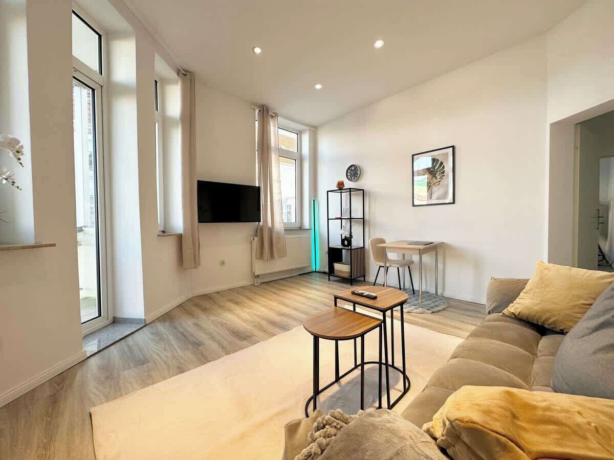 A modern living room with a sofa, a coffee table, a TV, and a dining area with a chair and table.