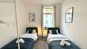 Una habitación pequeña y limpia con dos camas individuales, una ventana con cortinas y un radiador.