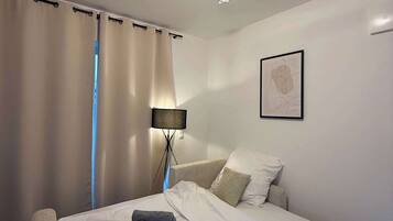 Een net opgemaakt bed met witte lakens, een lamp en een ingelijst kunstwerk aan de muur.