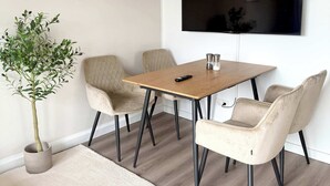 Un comedor moderno con una mesa de madera, cuatro sillas, una planta en maceta y un televisor de pantalla plana montado en la pared.